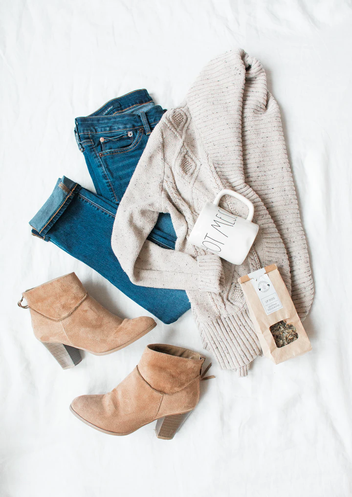 A flat-lay of jeans, a cream cardigan and tan ankle boots