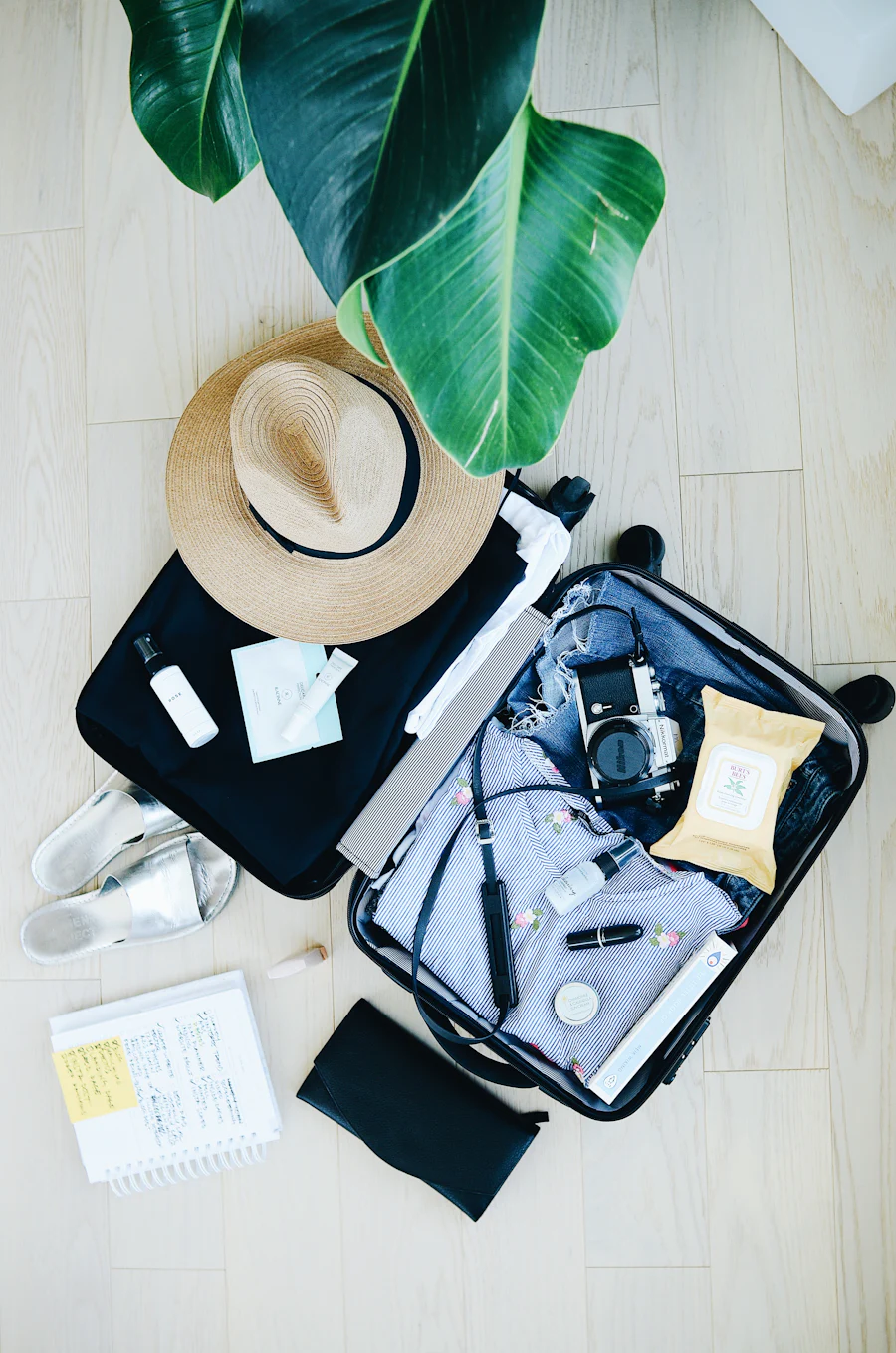 An open suitcase with a straw hat, shirts and travel essentials